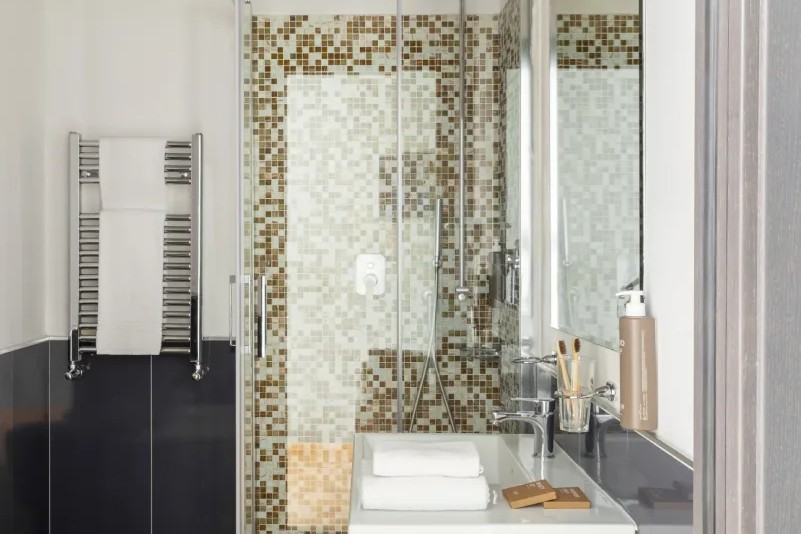 Modern bathroom with glass shower and mosaic tiles, sink with amenities and towels, functional design in Monti district Rome - Monti First, BZAR hotels in Rome