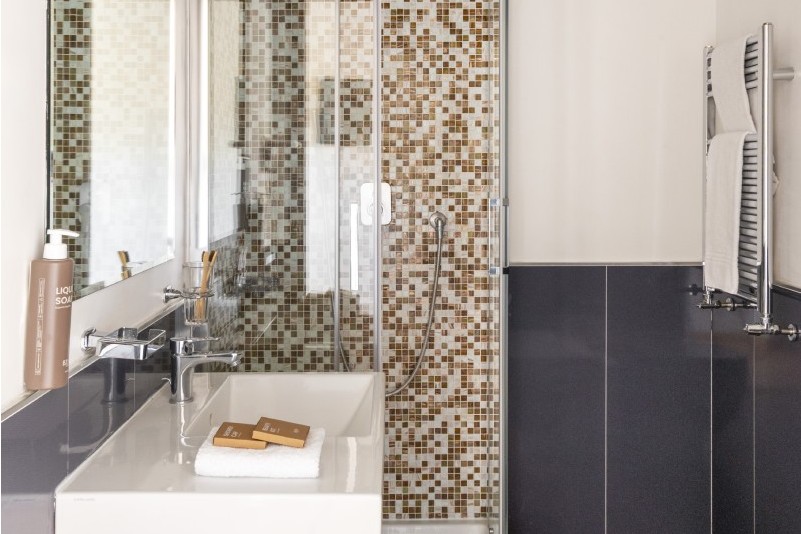 Modern bathroom with glass shower and mosaic tiles, sink with amenities and towels, functional design in Monti district Rome - Monti First, BZAR hotels in Rome