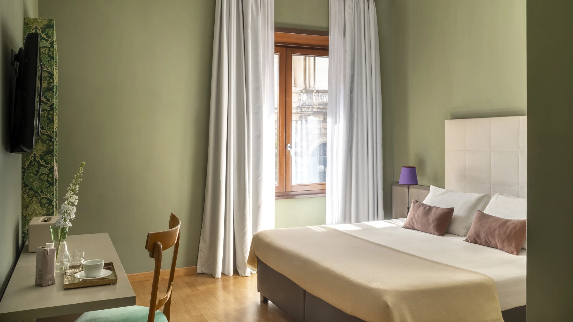 Bright standard room with double bed, green walls and large window overlooking historic building in Monti district - Monti First, BZAR hotels in Rome
            