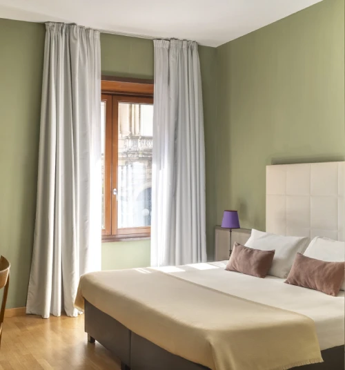 Bright standard room with double bed, green walls and large window overlooking historic building in Monti district - Monti First, BZAR hotels in Rome