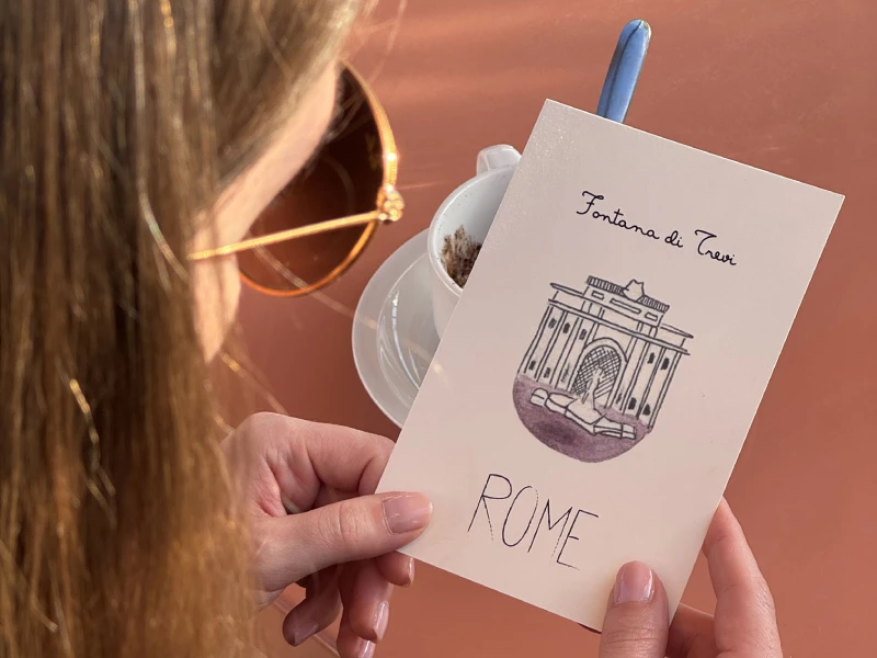 Traveler with coffee holding Trevi Fountain postcard, authentic moment in central Rome near Monti district - Monti First, BZAR hotels in Rome