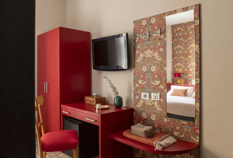 Small room with red desk, wall-mounted TV and decorative mirror, modern design in Monti district in Rome - Monti First, BZAR hotels in Rome