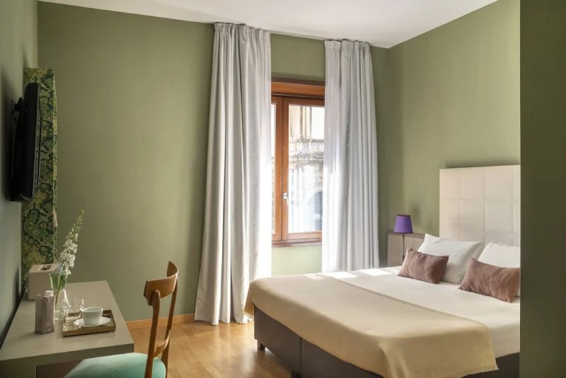 Bright standard room with double bed, green walls and large window overlooking historic building in Monti district - Monti First, BZAR hotels in Rome